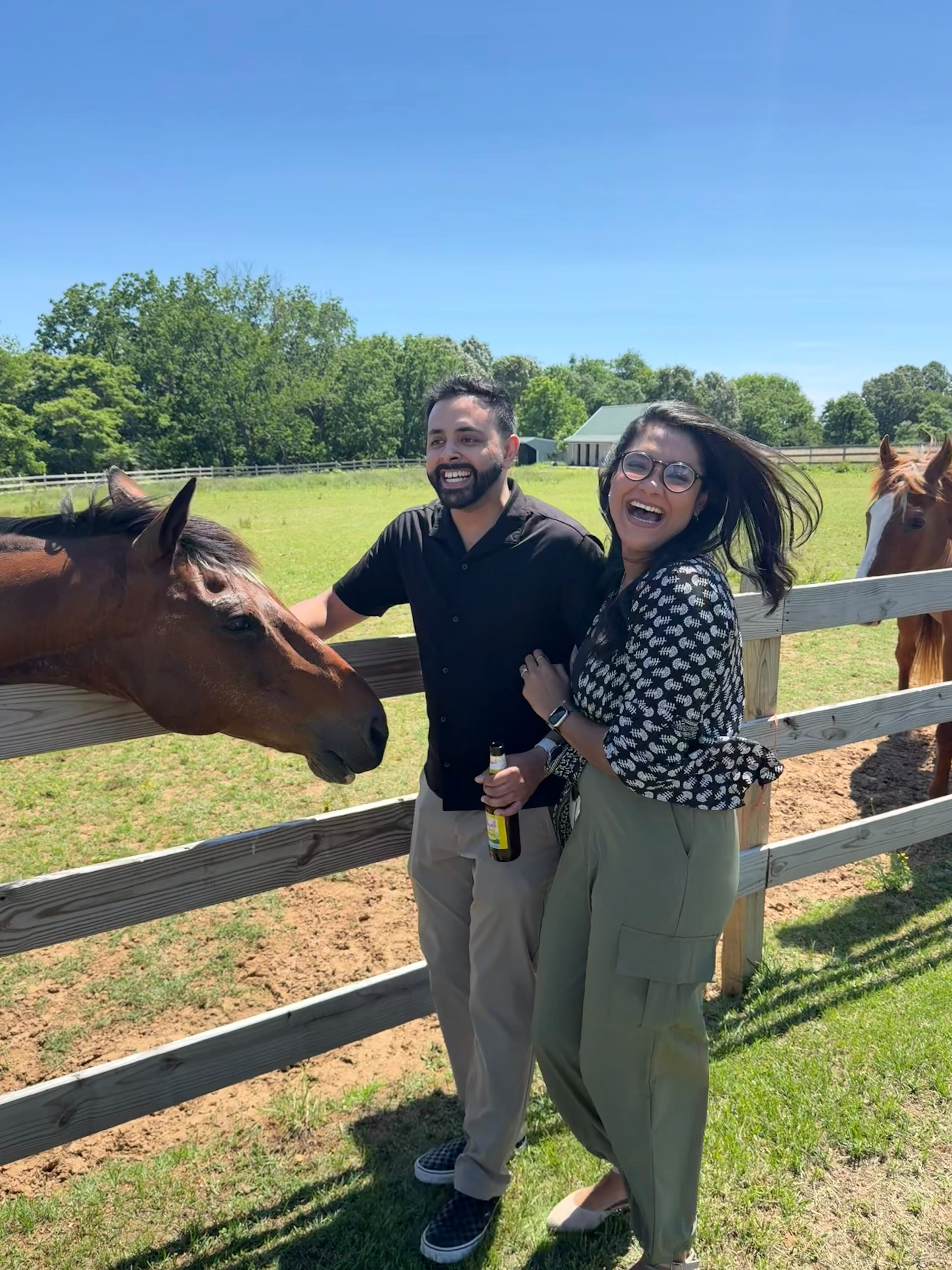 Kareena and Arvin laughing beside a horse on a sunny farm