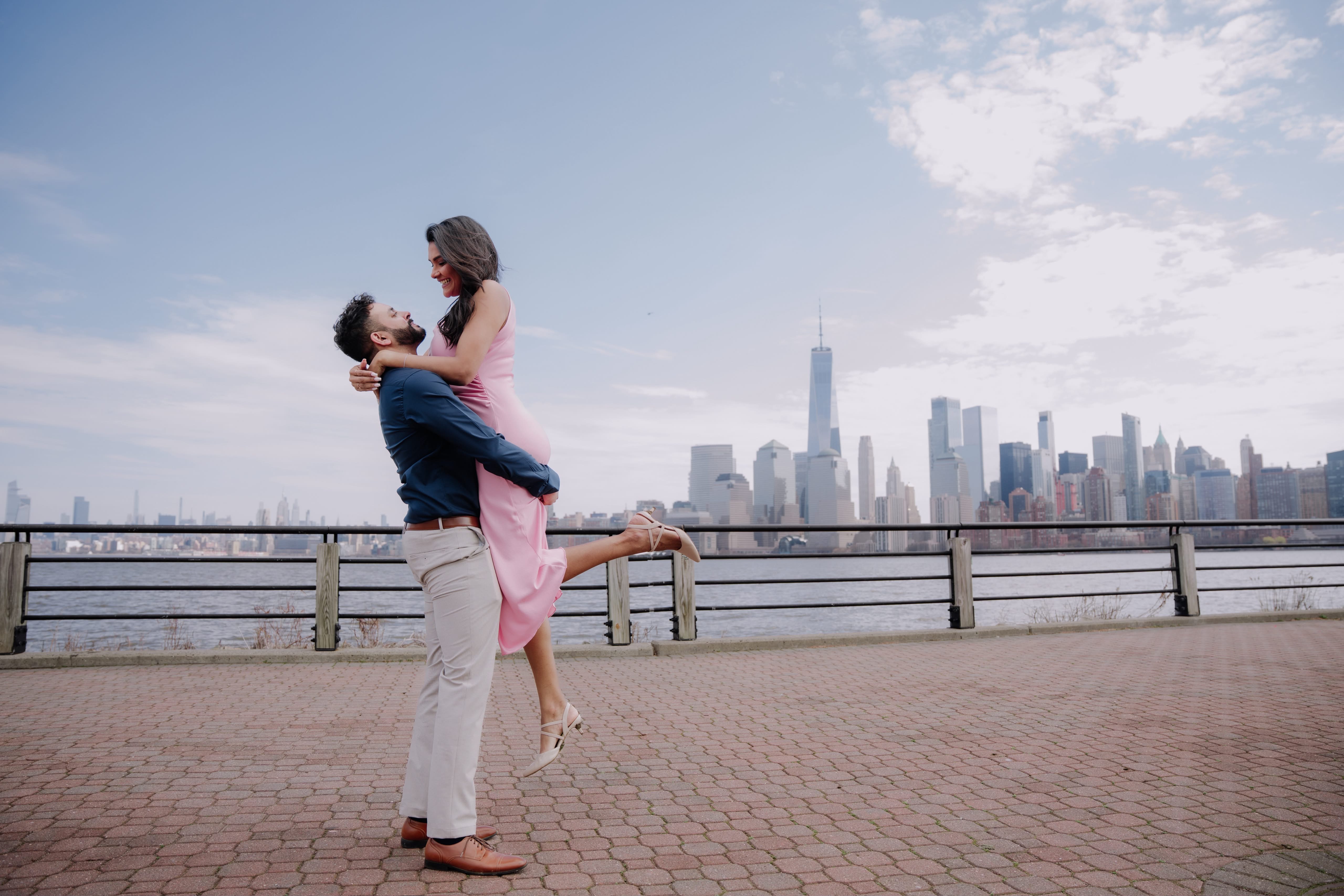 Kareena and Arvin embracing along the waterfront with the Manhattan skyline behind them